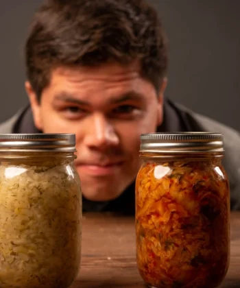A man curiously examining four jars of fermented vegetables, including sauerkraut, on a wooden table. A green banner in the top left corner reads 'Best Sauerkraut for Gut Health.