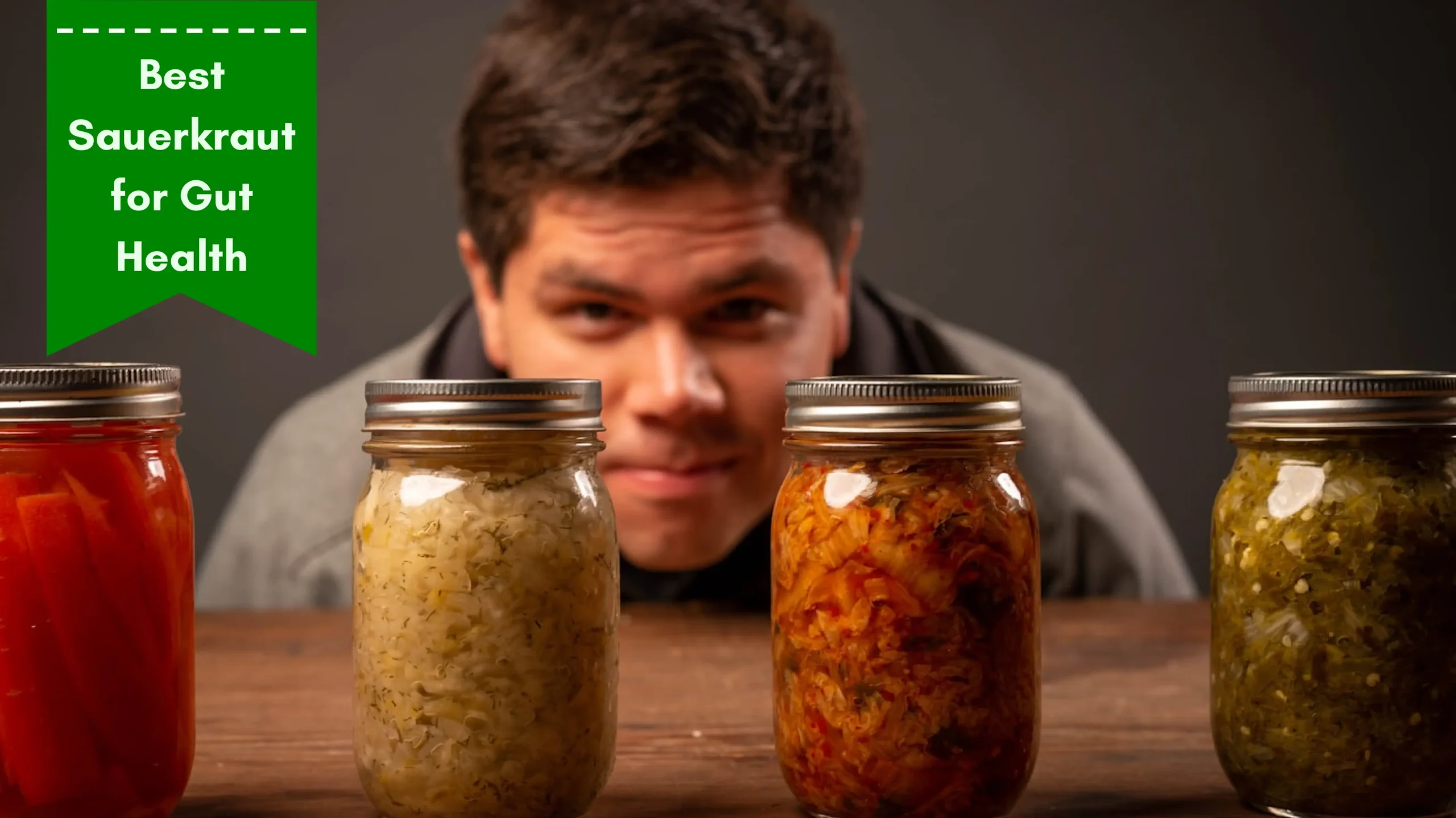 A man curiously examining four jars of fermented vegetables, including sauerkraut, on a wooden table. A green banner in the top left corner reads 'Best Sauerkraut for Gut Health.