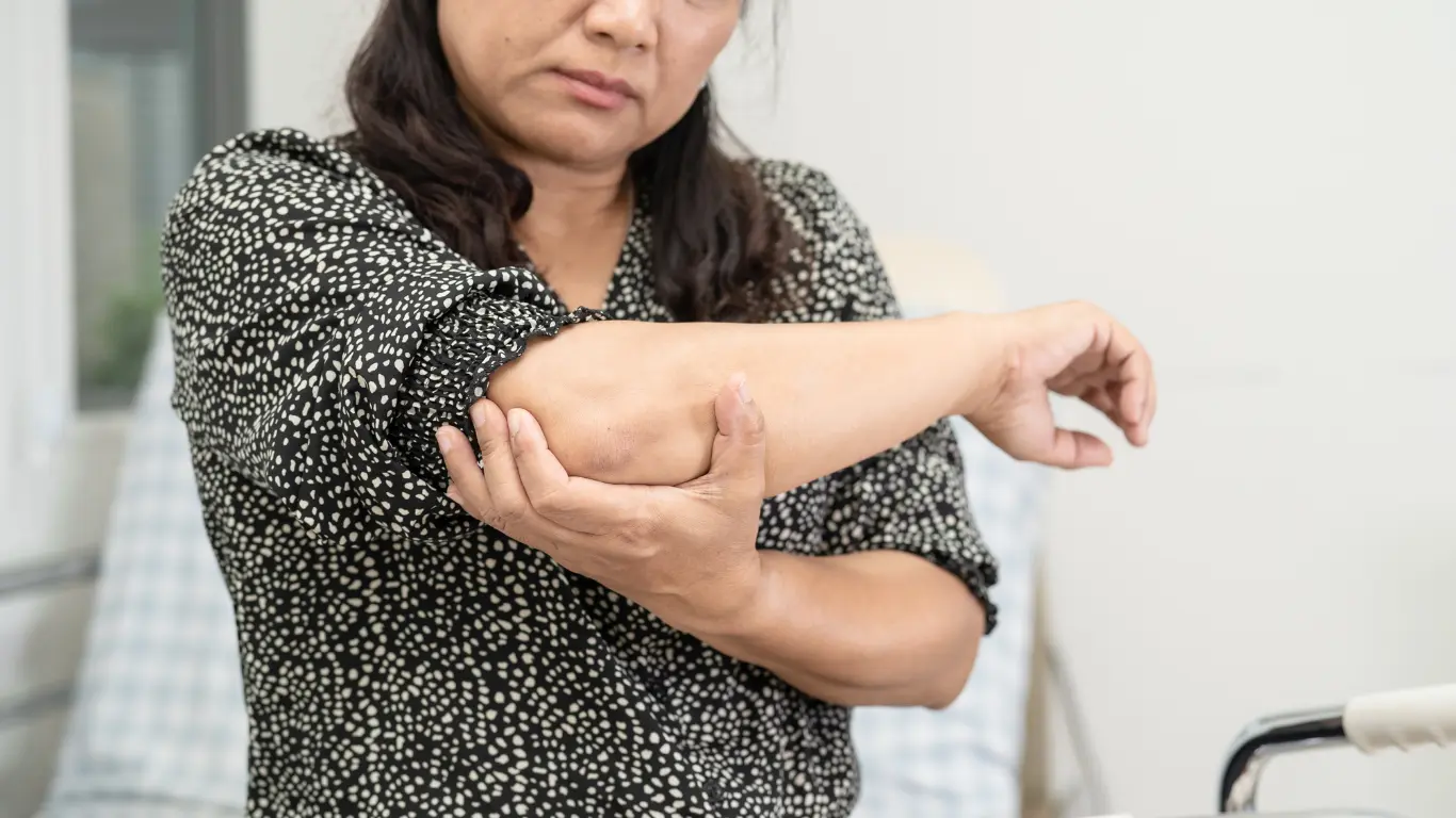 Middle-aged woman holding her painful elbow, possibly experiencing symptoms of a hyperextended elbow.