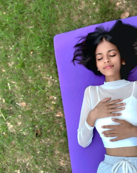 A women practicing yoga outdoors on a purple mat with eyes closed and hands on heart